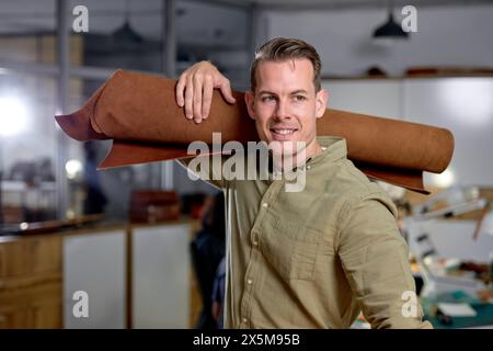excited smiling shoemaker holds set of leather. business and entrepreneur concept. Handmade craft production of leather goods.Leather shop. Sale of skin in rolls. Stock Photo