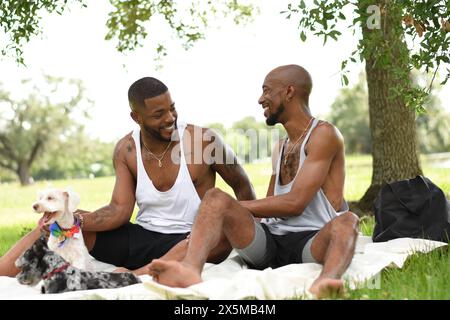 USA, Louisiana, Smiling gay couple with dogs having picnic on lawn in park Stock Photo