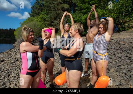 Group of friends in swimsuits stretching on rocky lakeshore, Yorkshire, UK Stock Photo