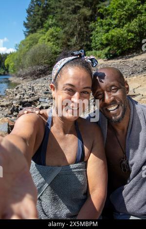 Portrait of smiling couple wrapped in towels on lakeshore, Yorkshire, UK Stock Photo