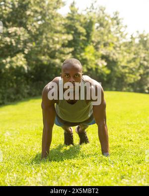 Athletic man doing push-ups on lawn in park Stock Photo