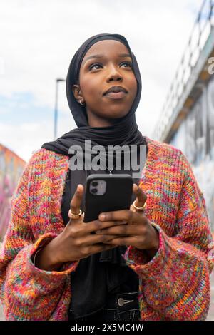 Young woman wearing hijab holding smart phone outdoors Stock Photo
