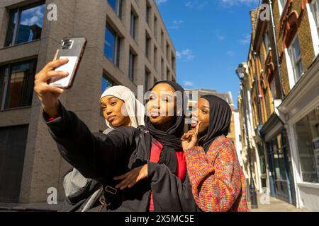 Smiling young women wearing hijabs taking selfie in city Stock Photo