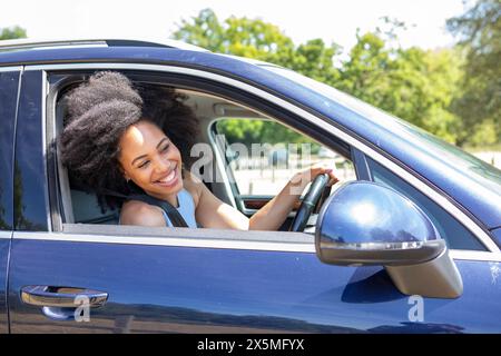 Young woman driving car, leaning out of window Stock Photo