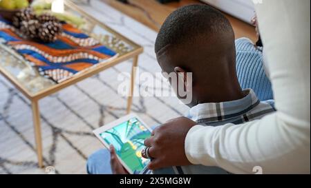 Mother and son (8-9) playing game on tablet at home Stock Photo