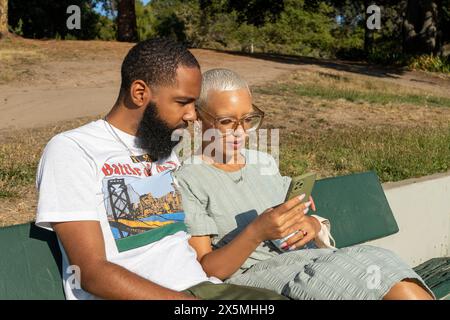 Couple sitting on bench and using smart phone Stock Photo