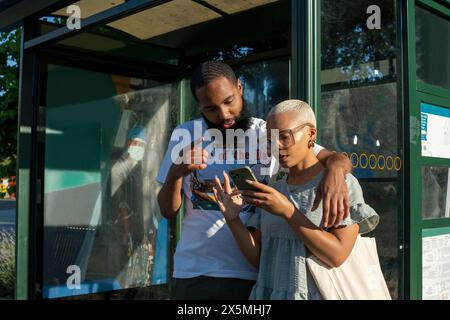 Couple waiting at bus stop and using smart phone Stock Photo