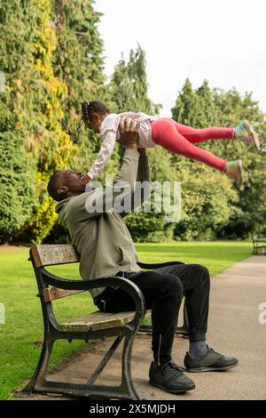 Smiling man playing with daughter on bench in park Stock Photo