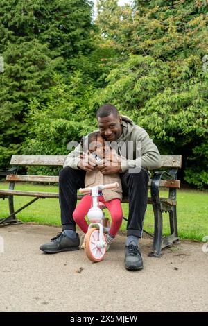 Portrait of smiling man with daughter on bench in park Stock Photo