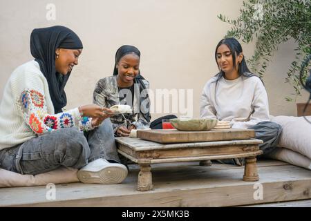 Friends wearing hijabs enjoying snacks on patio Stock Photo
