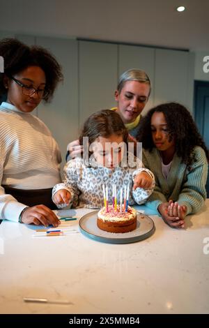 Mother assisting daughters preparing small birthday cake at home Stock Photo