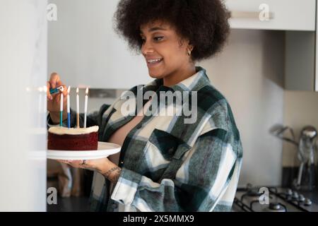 Woman lighting candles on birthday cake Stock Photo