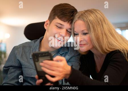 Mother using smartphone with disabled son Stock Photo