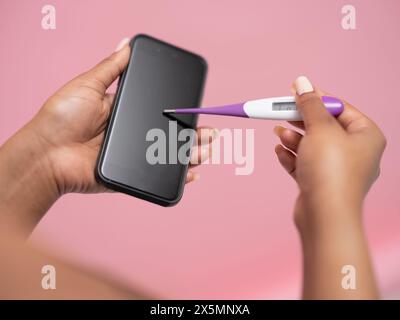 Close-up of womans hand holding thermometer and smart phone Stock Photo