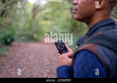 Man using compass in smart phone while hiking in forest Stock Photo
