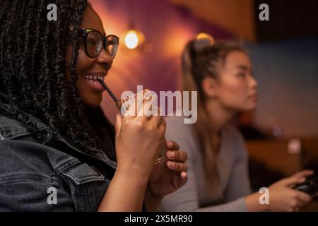 Young woman drinking cocktail while playing with friend in video games at pub Stock Photo