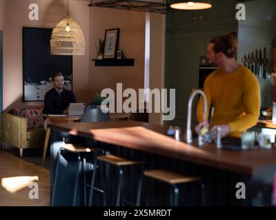 Man washing dishes while boyfriend using digital tablet at home kitchen Stock Photo