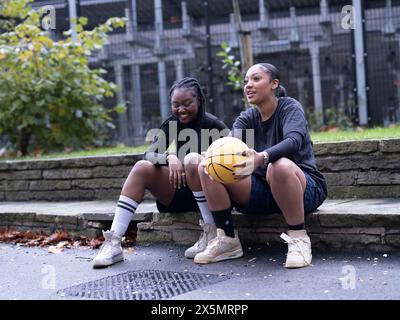 Two female friends sitting outdoors with basketball Stock Photo