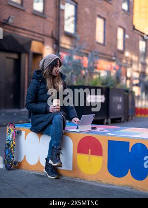 Woman using digital tablet while sitting on wall in city street Stock Photo