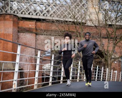 Smiling athletic man and woman jogging on footbridge Stock Photo