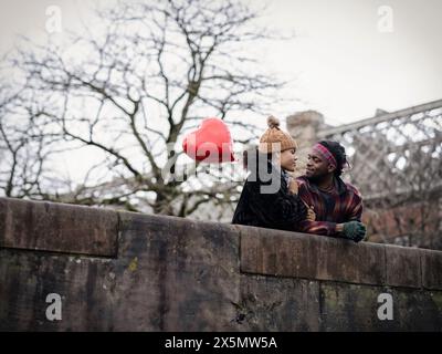 Smiling couple with heart shaped balloon leaning on wall Stock Photo