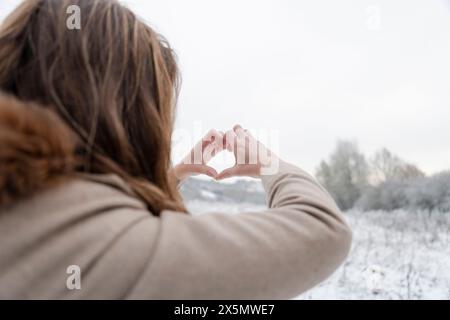 Rear view of woman making hand heart sign in winter landscape Stock Photo