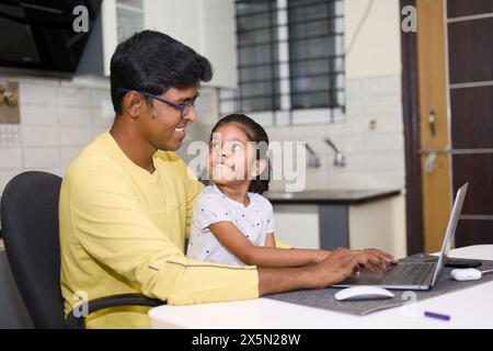 This image is about A indian father and daughter using laptop at home in the living room father wearing eyeglass Stock Photo