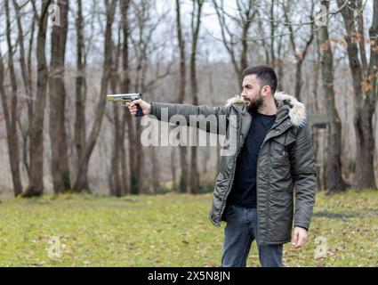 Young man aims and shoots with a gun in the forest Stock Photo