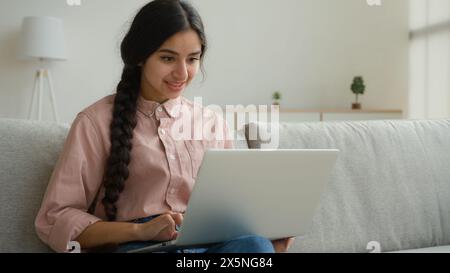 Smiling Arabian woman girl typing laptop at home working in quarantine Indian businesswoman student studying online e-learning business internet Stock Photo