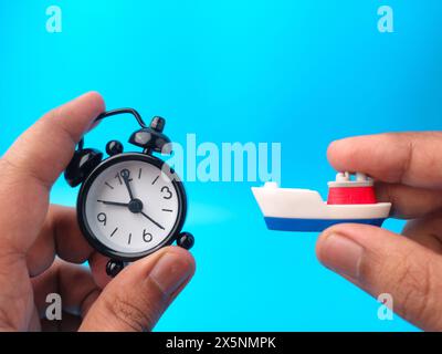 Hand holding clock and toy ships on blue background. Travel concept. Stock Photo