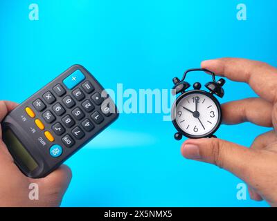 Hand holding black alarm clock and calculator on a blue background. Business concept idea. Stock Photo