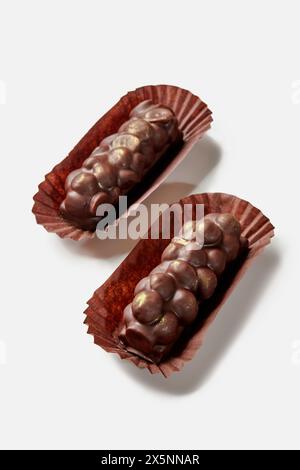 Two artisan dark chocolate bars with hazelnuts in brown paper wrappers presented on white surface, showcasing luxury confectionery Stock Photo