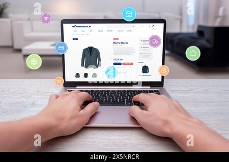 Hands typing on laptop, shopping online for men's blazer with levitating shopping icons. Modern concept of digital shopping convenience Stock Photo
