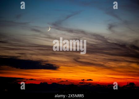 Red-orange sky at sunset in twilight evening with dark clouds and moon. Nature sky. Background, horizon golden sky, sunrise cloud magnificent. Stock Photo