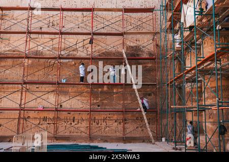 workers in lab coats on scaffolding work to restore and preserve the stone temple walls at Medinet Habu in Luxor, Egypt Stock Photo