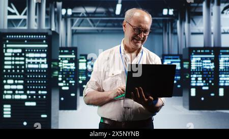 Capable serviceman expertly managing data while navigating in industrial server room. Proficient repairman in high tech facility ensuring optimal cybersecurity protection, optimizing systems Stock Photo