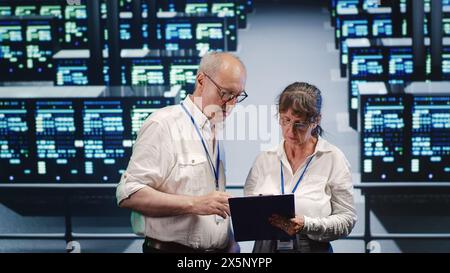 Cloud computing business executives looking around data center, using clipboard to crosscheck disaster recovery plan and assess high tech workplace servers in need of replacement, preventing concerns Stock Photo