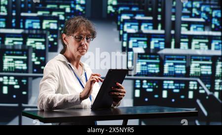 Precise serviceman in cloud computing company housing high end servers capable of quickly and efficiently performing complex computations and data analysis, using tablet to root out blips Stock Photo