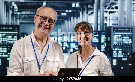 Colleagues in data center using laptop to monitor energy efficient rigs. Server farm using renewable sources employed to minimize consumption and reduce overall facility carbon footprint Stock Photo