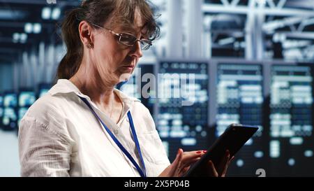 Aged technician working in data center housing GPU dedicated blade servers that can process artificial intelligence tasks with high efficiency, fixing faulty electronics used for machine learning Stock Photo