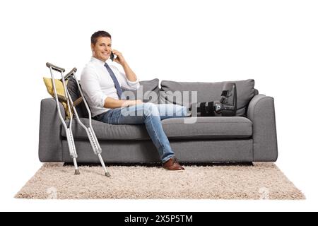 Businessman with a foot injury and leg brace sitting on a sofa and using a smartphone isolated on white background Stock Photo
