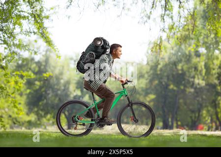 Full length profile shot of a guy with a backpack riding a bicycle in a park Stock Photo