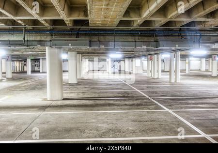 empty paid underground car parking, concrete poles artificial cool neon lights standard bay size Stock Photo