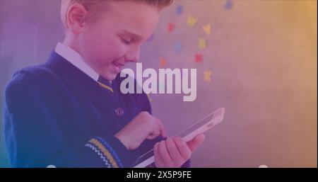 In school, boy in uniform using a tablet, colorful letters on wall behind Stock Photo