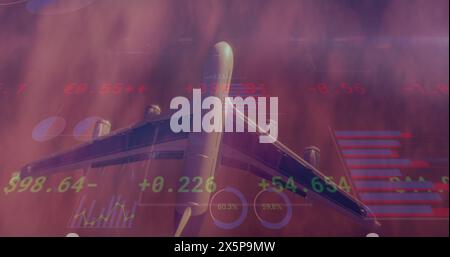 Image of charts and financial data processing over aeroplane flying in cloudy sunset sky Stock Photo