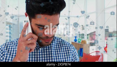 Image of connected icons over biracial man looking at digital tablet and talking on cellphone Stock Photo