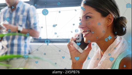 Image of icons connected with lines over smiling caucasian woman talking in cellphone at office Stock Photo