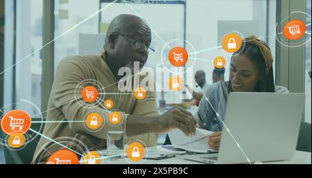 Image of connected icons over diverse coworkers discussing reports on laptop in office Stock Photo