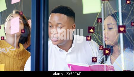 Image of two globes of digital icons over diverse office colleagues discussing over memo notes Stock Photo