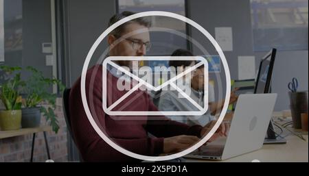 The man is working on his laptop in the office, while his coworkers are busy in the background Stock Photo